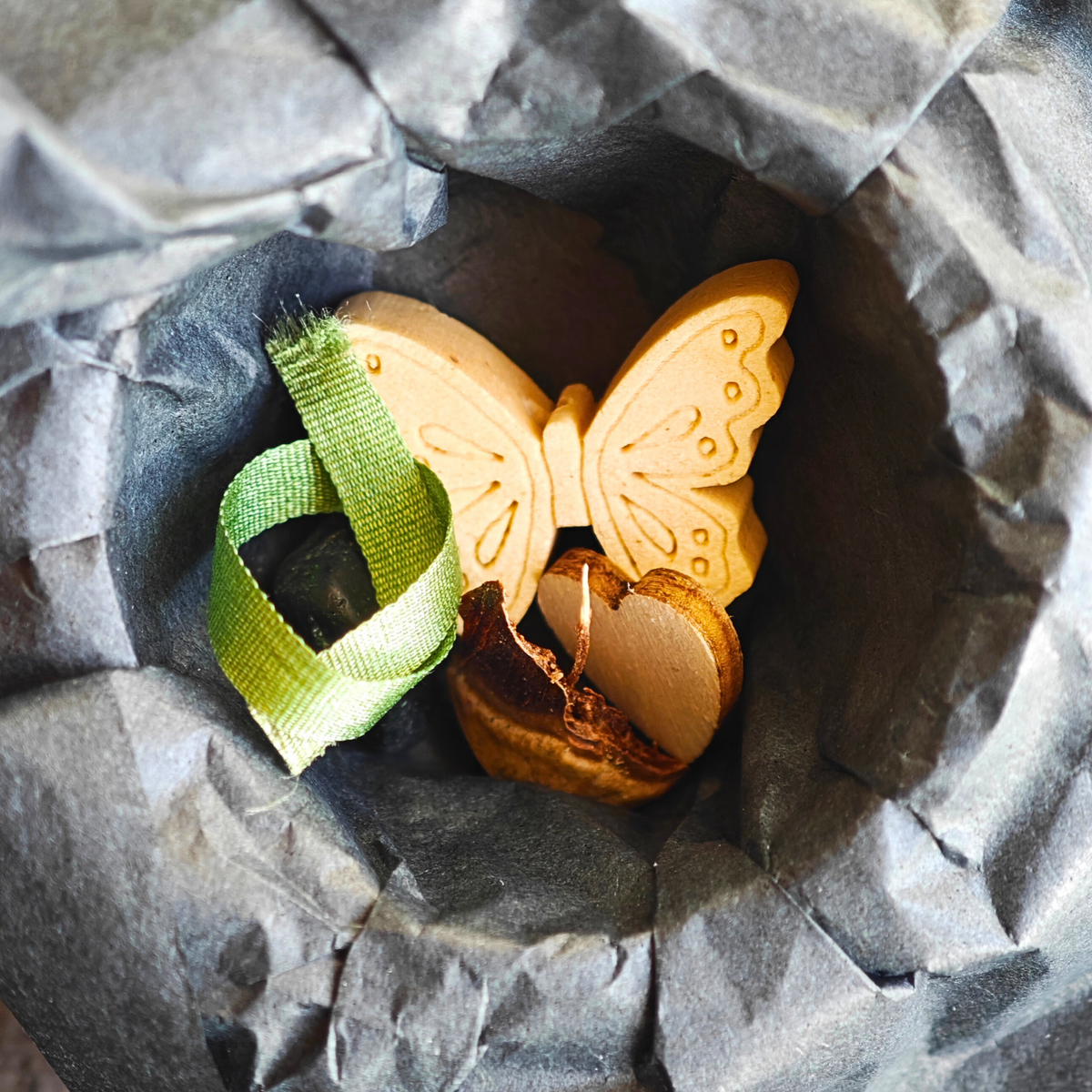 Geöffnete MEMENTOVIA-Box mit Seide, Herz, Obsidian, Schmetterling und Tanne – symbolische Beigaben für Trost, Liebe und bleibende Erinnerung. Die Beigaben liegen auf schwarzem Seidenpapier.